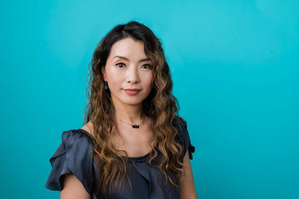 An Asian woman poses against a turquoise blue background.