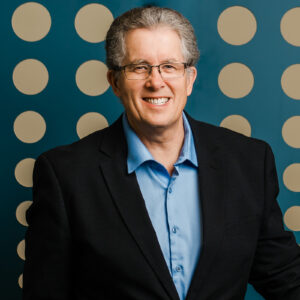 Stephen Yakimets of RGO wearing a black blazer and a blue shirt with modern blue office interiors